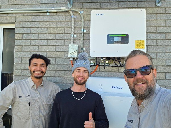 Happy customer giving a thumbs up with the SEQ EV Chargers crew beside a SOFAR solar inverter and battery
